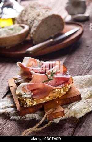 Bruschetten mit Frischkäse, Prosciutto und Rosmarin auf Schneidebrett und Holztisch Stockfoto