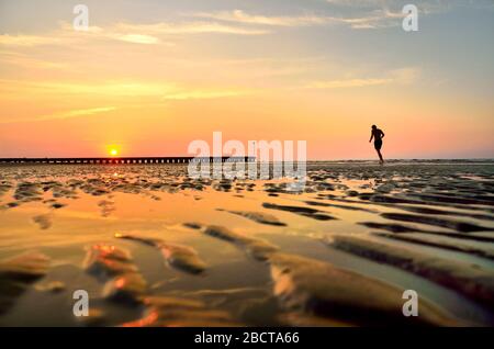 Silhouette des jungen Mannes, der bei Sonnenaufgang auf Strandsand läuft. Originaltapete aus dem aktiven Sommerurlaub. Stockfoto
