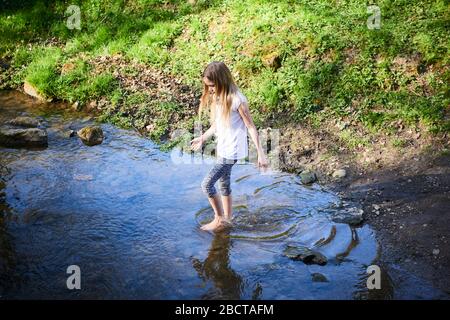 Kind niedlich mutig blonde Mädchen spielen in der Creek. Tapferes Mädchen zu Fuß in Waldbach und die Natur erkunden. Sommer Kinder Spaß. Kinder Sommer Stockfoto