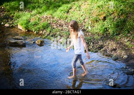 Kind niedlich mutig blonde Mädchen spielen in der Creek. Tapferes Mädchen zu Fuß in Waldbach und die Natur erkunden. Sommer Kinder Spaß. Kinder Sommer Stockfoto