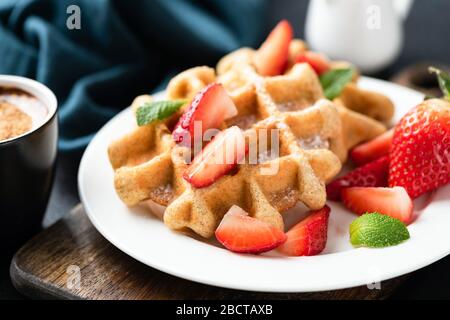Belgische Waffeln mit Erdbeeren und Süßwaren auf weißem Teller mit Minzblatt. Nahansicht. Leckeres süßes Frühstück Stockfoto