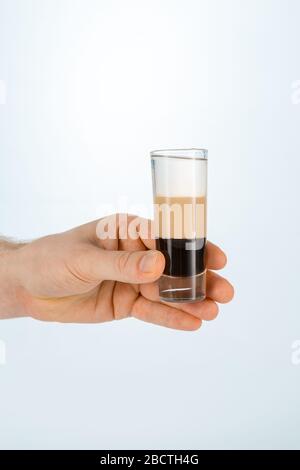 Nahaufnahme einer Hand, die ein Glas B52-Cocktail auf weißem Hintergrund mit Kopierraum hält. Stockfoto