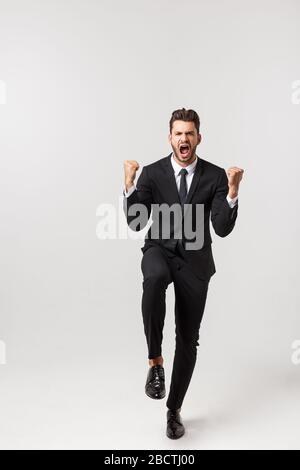 Fröhliche junge bärtige Geschäftsleute zeigen aufgeregt mit geklonten Fäusten. Ganzer Portrait Business man isoliert über weißem Studiohintergrund Stockfoto