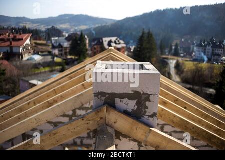 Close-up Detail der Dachrahmen aus grobem Holz Bauholz Balken und Schornstein aus Schaumstoff Isolierung Blöcke auf verschwommen grünen Hintergrund. Gebäude, Dach, Stockfoto