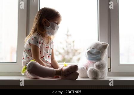 Trauriges Kind und sein Teddybär beide in schützenden medizinischen Masken. Kinder und Krankheit COVID-2019 Krankheitskonzept Stockfoto