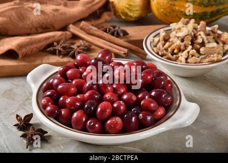 Eine Schüssel mit frischen Preiselbeeren mit Sternanis, Zimtstäbchen, gehackten Walnüssen und Weihnachtswürzen Stockfoto