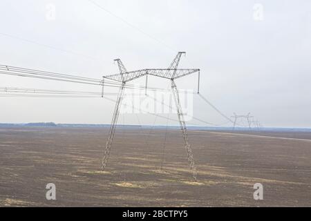 Große Metallstützen von Stromleitungen, die durch agrarische Felder zum Horizont führen. Stockfoto