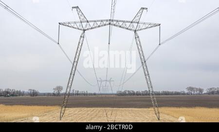 Große Metallstützen von Stromleitungen, die durch agrarische Felder zum Horizont führen. Stockfoto