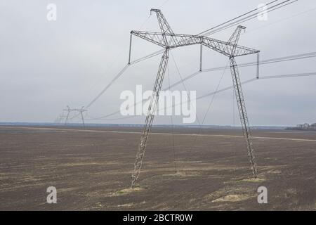 Große Metallstützen von Stromleitungen, die durch agrarische Felder zum Horizont führen. Stockfoto