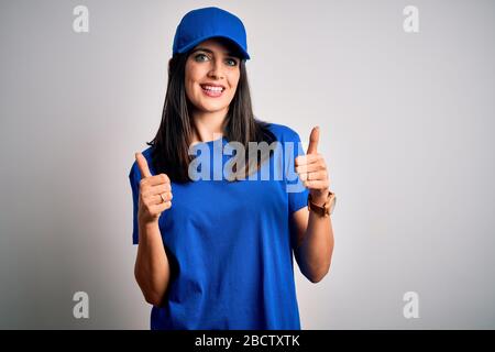 Junge Aushänderin mit blauen Augen, die eine Kappe trägt, die über blauem Hintergrund steht, die mit der Hand positive Geste macht, mit den Daumen lächelnd und hap Stockfoto