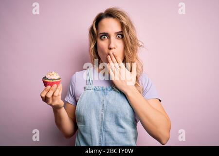 Junge schöne blonde Frau Eatimg Schokoladenkuchen über isoliertem rosa Hintergrund Deckelmund mit der Hand schockiert aus Scham aus Fehler, Ausdruck o Stockfoto