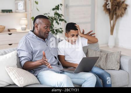 Schwarzer Mann und sein Enkel schauen schockiert auf den Laptop-Bildschirm Stockfoto