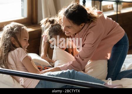 Fröhliche junge Mixed-Race-Frau, die mit Kindern im Schlafzimmer spielt. Stockfoto