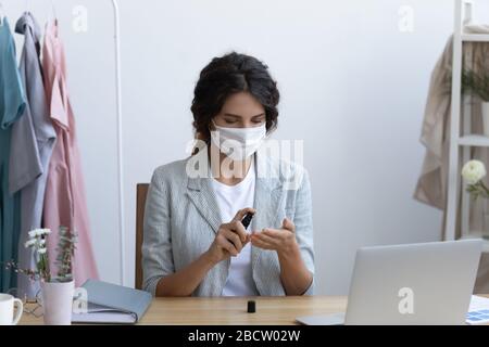 Junge Frau in schützender medizinischer Maske, die Hände mit Antiseptikum desinfiziert. Stockfoto