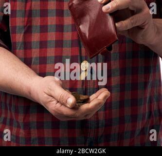 Der Mann in einem roten Hemd gießt Hryvnia-Münzen aus einer braunen Ledertasche in seine Hand, Armutskonzept Stockfoto