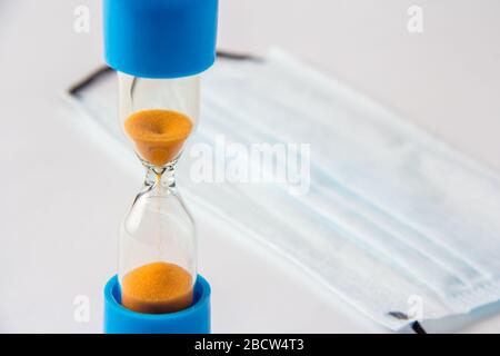 Medizinische Maske und Sanduhr auf weißem Hintergrund. Stockfoto