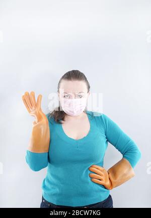 kaukasische Hausfrau mittleren Alters trägt eine schützende medizinische Maske und große Gummihandschuhe für Sterilität auf weißem Hintergrund, eine Frau in einem Haus-Pullover Stockfoto