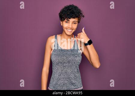 Junge schöne afro-amerikanische afro-Sportlerin, die Sport macht, Sportswear trägt lächelnd Telefongeste mit Hand und Fingern, wie man spricht Stockfoto