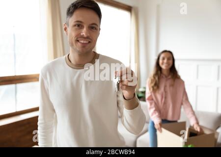 Lächelnder junger kaukasischer Mann, der Schlüssel vorführt, Immobilienkauf. Stockfoto