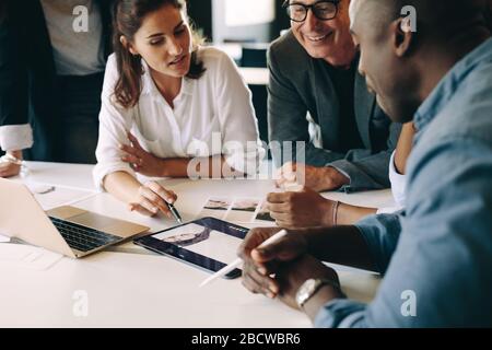Geschäftsleute, die sich Fotos auf einem digitalen Tablet ansehen und über Design-Inspiration sprechen. Kreative Unternehmensgruppe, die eine Besprechung abhält. Stockfoto