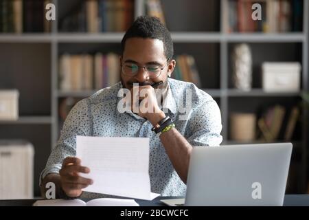 Nachdenklicher afroamerikanischer Mann liest Brief im Amt Stockfoto