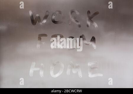 Die Worte arbeiten von zu Hause aus handschriftlich auf nassem Fensterglas Bei Tag: Nahaufnahme des Vollformatsbildes mit selektivem Fokus Stockfoto