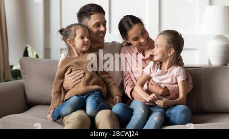 Lächelndes Familienpaar, das niedliche Töchter auf dem Schoß hält. Stockfoto