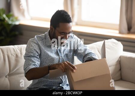 Aufgeregter birazialer Mann entpackt das Paket für die Internetlieferung Stockfoto