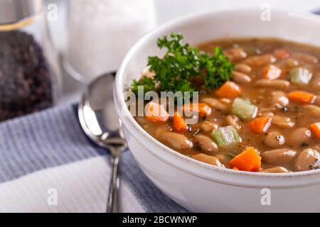 Nahaufnahme von leckerer Bohnensuppe mit Karotten und Sellerie in einer weißen Schüssel Stockfoto