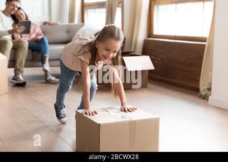 Überfreuliches kleines Mädchen, das Kartons in ein neues Haus schiebt. Stockfoto