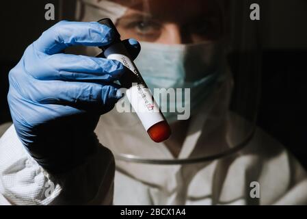 Arzt in medizinischen Anzug mit Schild hält in der Hand Covid-19-Test zeigt positive auf Coronavirus Stockfoto