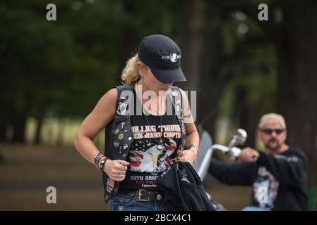 Eine kaukasische, blonde Frau bei einem Rolling Thunder Event, die eine schwarze Mütze und schwarze Kleidung mit Kriegsemblemen trägt. Ein Biker ist im Hintergrund. Stockfoto