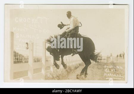 Crockett Riding Mount Toro Salinas Rodeo, Im Jahr 1919. Diese echte Postkarte zeigt ein Bild eines Mannes, der auf einem Pferd im Salinas Rodeo reitet. Der Mann steht zu Pferd in der Nähe des weißen Zauns, der die Rodeo-Arena umrahmt. Er hält einen Hut in der rechten Hand. Crockett Riding Mount Toro Salinas Rodeo, Im Jahr 1919 Stockfoto
