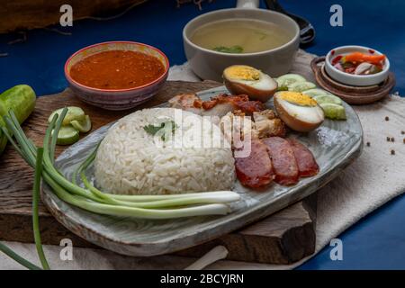 Rotes Schweinefleisch mit Reis (Kao Moo Dang): Rotes Grillpork im thailändischen Stil, Entenei und knuspriger Schweinebauch, geschnittene Gurke mit roter Soße und Brühe. Stockfoto