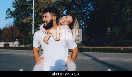 Bärtiger Mann in weißer Kleidung, der sein Mädchen trägt und draußen auf der Straße lächelt Stockfoto