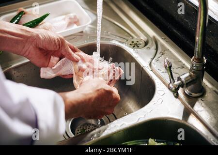 Hände des Mannes spülen den Hähnchenschenkel unter Leitungswasser Stockfoto