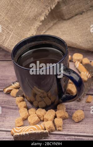 Dunkelblauer Teebecher aus Keramik, Plätzchenstäbchen mit Schokolade und weiße Vereisung auf Holzhintergrund. Nahaufnahme Stockfoto