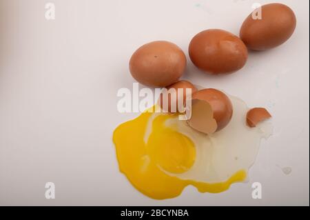 Ein zerbrochenes Hühnerei und verstreute Eier auf weißem Grund. Nahaufnahme Stockfoto