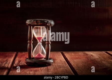Das Konzept der Zeit läuft aus. Eine Sanduhr mit durchfallendem Sand, auf dunklem Holzhintergrund mit Kopierraum Stockfoto