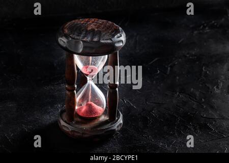Das Konzept der Zeit läuft aus. Eine Sanduhr mit durchfallendem Sand auf schwarzem Hintergrund mit Kopierbereich Stockfoto