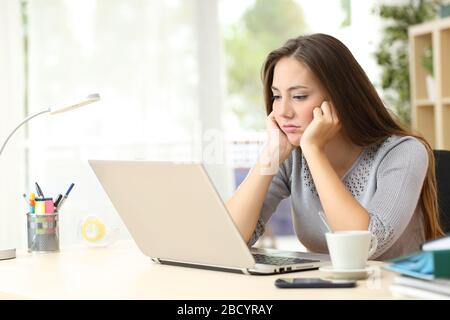 Gelangweilte Unternehmerin, die einen Laptop-Bildschirm auf einem Schreibtisch zu Hause betrachtet Stockfoto