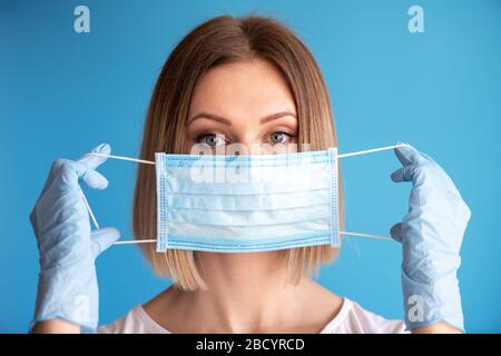 Arzt oder Pfleger halten sich in der Hand, mit Handschuhverschluss Gesichtsmaske auf blauem Hintergrund. Medizinisches und medizinisches Konzept, um die Verbreitung des Virus zu verhindern Stockfoto
