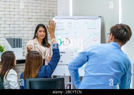 Rückansicht der asiatischen Geschäftsfrau, die Hand aufwirft, um dem Sprecher Fragen zu stellen, wenn er im Kreativbüro, in der Privatausbildung und im Seminar zusammenkommt, Partner an Stockfoto