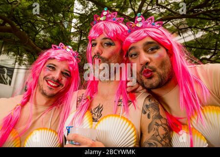 Eine Gruppe von Männern, die sich als Frauen verkleidet haben, rosa Perücken tragen und lächeln, während des Karnevals tagsüber auf den Straßen feiern Stockfoto