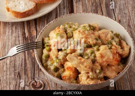 Hähnchenfilet mit grünen Erbsen, die in einer cremigen Soße auf einem Holztisch gedünstet sind Stockfoto