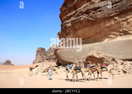 Beduinen in traditioneller Kleidung mit Wohnwagen von Kamelen in der Wüste Wadi Rum, Jordanien, Naher Osten. UNESCO-Weltkulturerbe Stockfoto