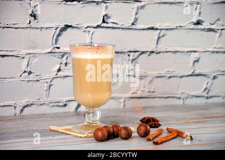 Gläserner Latte Becher an einer Serviette, neben Zimtstäbchen, Anis und Macadamia-Nüssen. Stillleben Nahaufnahme. Stockfoto