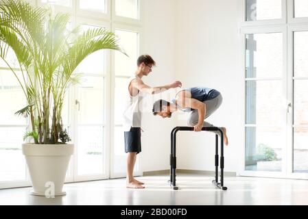 Zwei Männer, die mit einem Mann Kalisthenics Workout durchführen, der den anderen bei planschen Übungen an parallelen Bars in einer Gesundheits- und Fitness-Konce hilft Stockfoto
