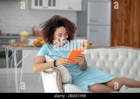 Junge Frau mit Tablette, die sich zu Hause auf einer Couch befindet. Stockfoto