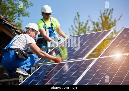 Zwei professionelle Techniker, die schwere Solar-Lichtschnur auf einer hohen Stahlplattform installieren. Installation von externen Solaranlagen, alternatives Konzept zur Erzeugung erneuerbarer grüner Energie. Stockfoto